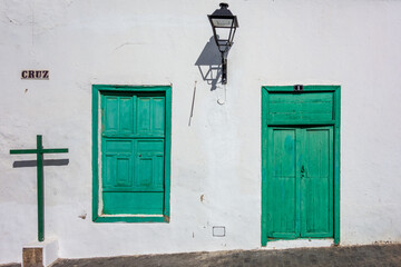 Fototapeta na wymiar White house with green door and window shutter, a cross with a street name sign 