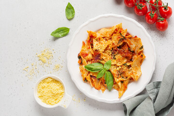 Pasta Maltagliati with classic tomato sauce, parmesan and basil on a rustic concrete light table background. Traditional Italian dish serving. Top view.