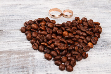 Close-up coffee beans and wedding rings on wood. Heart made of brown coffee seeds.