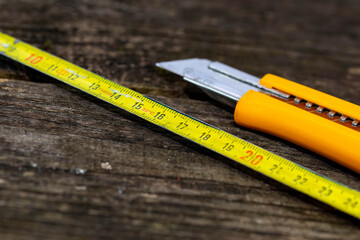 Old tape measurer, yellow utility knife on aged weatherd wood boards, space for text.