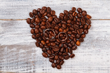 Heart made of coffee and wedding rings. White wood background.