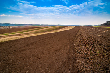 Fototapeta na wymiar arable spring field, plowed soil and relief hilly, landscape in the background