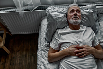 middle-aged man lying down in bed on pillow, having insomnia sleeping disorder. alone at home