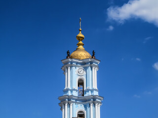 Golden dome on the blue bell tower of the Holy Transfiguration Cathedral in Sumy (Ukraine). Church tower with clock, sculptures and cross isolated on blue sky background