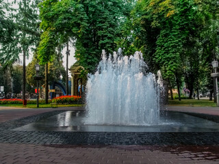 Naklejka premium Fountain Sugar in Pokrovsky Square in Sumy (Ukraine). Modern fountain with jets of water gushing from the floor against the backdrop of greenery and flowers in the park