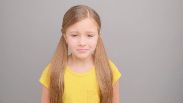 A little girl in a yellow T-shirt is crying and screaming. Picture taken in the studio on a gray background. Close-up portrait of a girl.