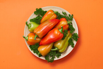 The colored pepper and parsley lie on a slide on a wooden plate on a orange background with text area.