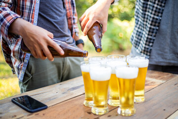 Pour the cold beer from the bottle into the glass on the wooden table.