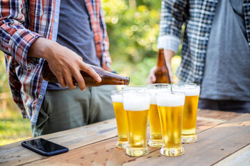 Pour the cold beer from the bottle into the glass on the wooden table.
