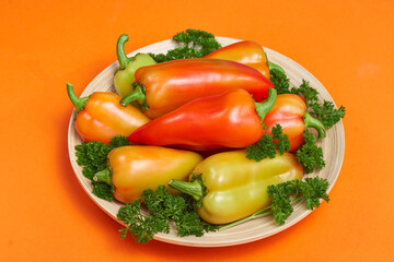 The colored pepper and parsley lie on a slide on a wooden plate on a orange background with text area. Close up view.