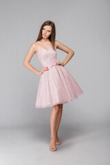 Young beautiful girl in a pink dress stands on a gray background