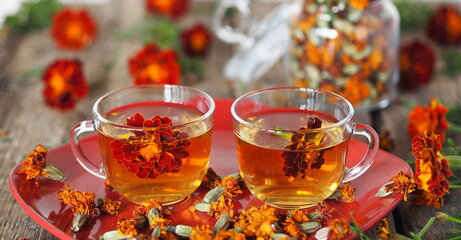 Autumn healing background. Tea cups with herbal tea with calendula flowers or Chernobrivtsi or Mary's Gold on a red plate on a vintage wooden background with dried flowers.