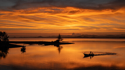 Fototapeta na wymiar A fisherman standing on a boat coming back from fishing in the sunset silhouettes orange sky