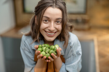 Portrait of pretty smiling woman with fresh brussels sprouts on the kitchen at home. Healthy cooking concept. High quality photo