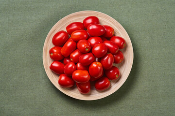 Whole small tomatoes in a wooden plate is on a green napkin close up view. The view from the top.