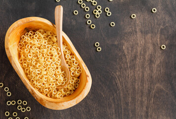 Anellini pasta in wooden olive bowl on old wooden background. Cooking concept. Top view with copy space.