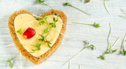Heart shaped mini canapes with butter, cheese and watercress micro greens on a white wooden background. View from above.