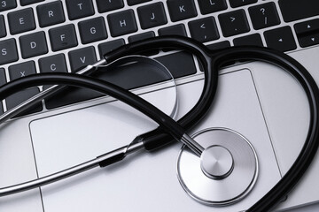 Computer repair, IT industry or modern medical service concept - top view of a black stainless stethoscope on a laptop keyboard.