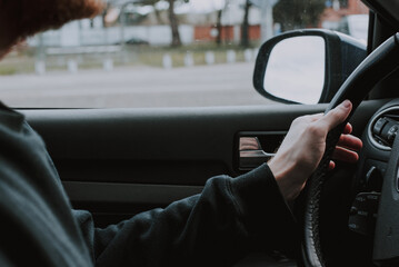 Detalle de un conductor joven en un coche con las manos en el volante. Se ve el espejo retrovisor del automóvil