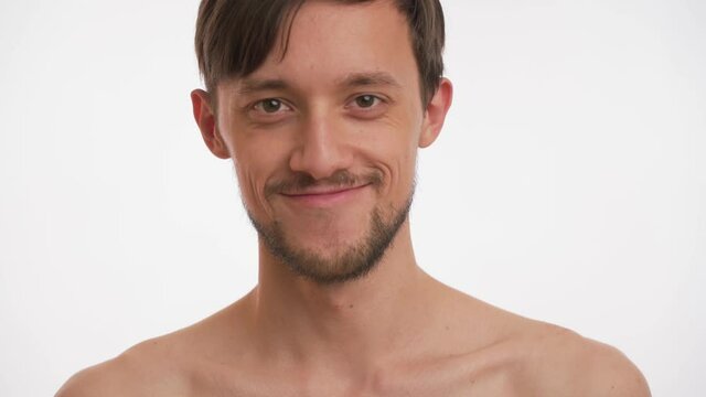 Single young pretty pleased Caucasian half naked brunette man with beard, moustache look at camera, smile isolated on white background. Close up view portrait of happy passionate male slow motion