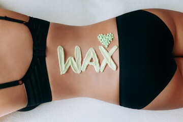 Top view on inscription wax laid out with hot wax for depilation. Heart which composed of granules of depilatory wax. Hair removal procedure on female back.