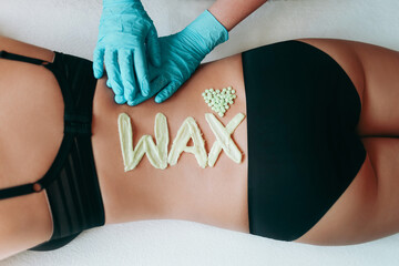 Top view on inscription wax laid out with hot wax for depilation. Hair removal procedure on female back. Heart which composed of granules of depilatory wax. The gloved hands of the depilation master. - obrazy, fototapety, plakaty