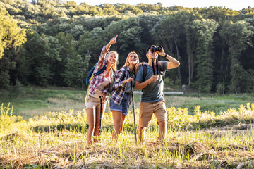 Group of friends hiking in nature.They walking through forest on beautiful sunset.Man using binoculars.	