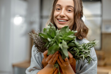 Portrait of cheerful woman in apron with fresh spicy herbs basil, rosemary, thyme on the kitchen....