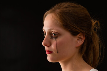 Upset female with tears falling from eyes from close up. Crying woman on dark background from profile. Young sad female with blurred mascara.