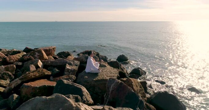 Mujer madura sentada en roca espig&oacute;n con postura zen  y dron orbitando