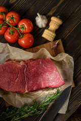 A piece of meat on a cutting board with tomatoes, spices and a knife.