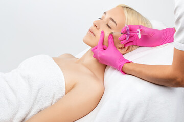 Cosmetologist makes rejuvenating anti wrinkle injections on the face of a beautiful woman. Female...