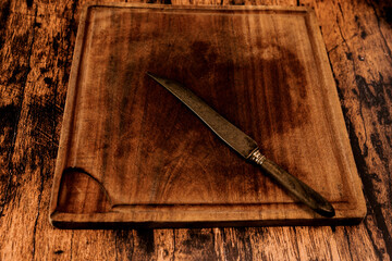 Worn wooden cutting board on an old worn wooden table with an old knife on it