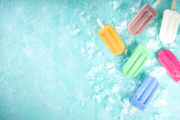 Selection of bright multicolored ice cream popsicle. Various gelato, frozen lollypops - chocolate vanilla blueberry strawberry pistachio orange, with crushed ice on light blue sunny background