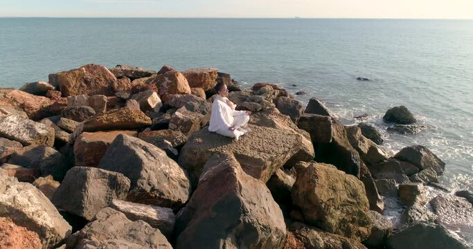 meditaci&oacute;n y yoga de mujer senior vestida de blanco junto al mar y dron sobrevol&aacute;ndola