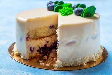 Homemade blueberry cut of cake decorated with white frosting, cream and fresh berries. Birthday or festive sponge pie isolated on blue background.
