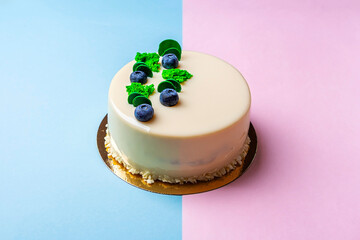 Homemade uncut blueberry vegan cake decorated with white frosting, cream and fresh berries. Birthday or festive sponge pie on two tone geometric background. Close up, copy space for text.