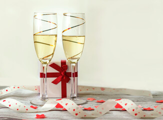 two golden glasses of champagne with a gift box and a red hearts ribbon