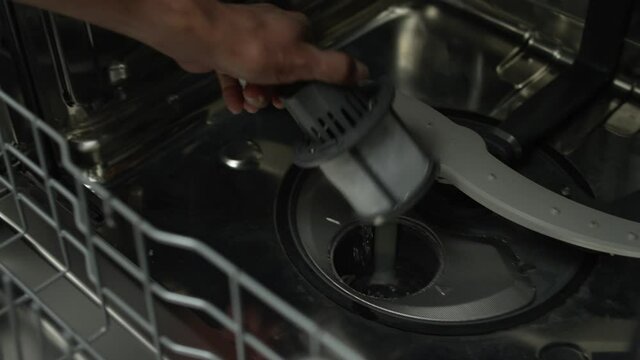 Man's hand removes the filter from the bottom of the dishwasher in the kitchen