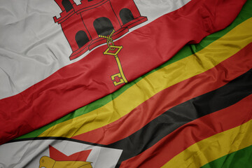waving colorful flag of zimbabwe and national flag of gibraltar.