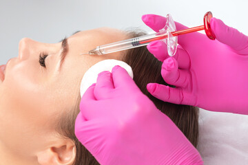 Cosmetologist makes rejuvenating anti wrinkle injections on the face of a beautiful woman. Female...