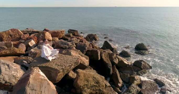 vuelo a&eacute;reo sobre bella mujer madura sentada meditando junto al mar