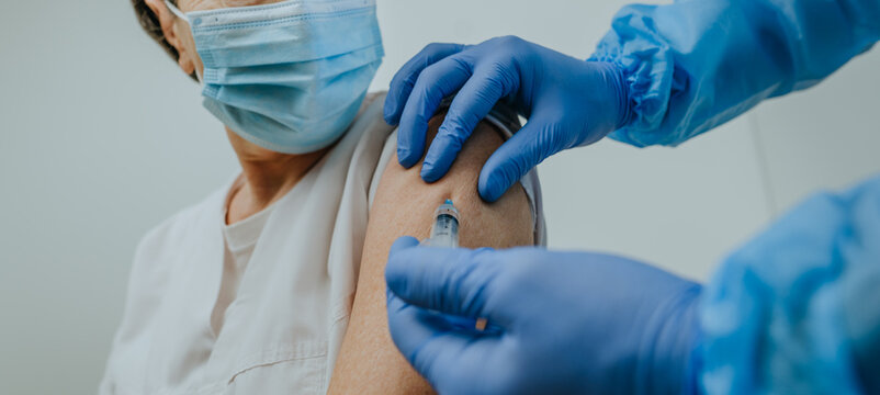 Close up of doctor in protective overall and gloves making COVID-19 vaccination