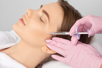 Cosmetologist makes rejuvenating anti wrinkle injections on the face of a beautiful woman. Female...