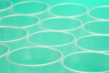 Close up of a group of empty translucent plastic cups, ordered on a turquoise colored surface.