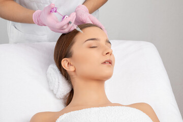 Cosmetologist makes rejuvenating anti wrinkle injections on the face of a beautiful woman. Female...