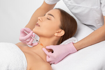 The beautician makes rejuvenating anti wrinkle injections on the face and neck of a beautiful...