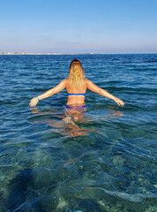 A woman with blonde hair enters the turquoise water in a bathing suit