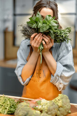 Portrait of cheerful woman in apron with fresh spicy herbs basil, rosemary, thyme on the kitchen....