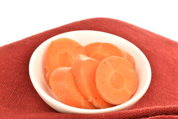 Several slices of ripe organic, unpeeled carrots in a white ceramic saucer on a red linen napkin, close-up, isolated on white.